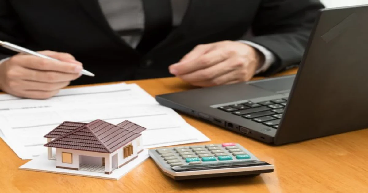 صورة تعبر عن مراجعة مستندات التمويل أو الحسابات العقارية مع حاسوب محمول وآلة حاسبة ونموذج منزل على مكتب عمل