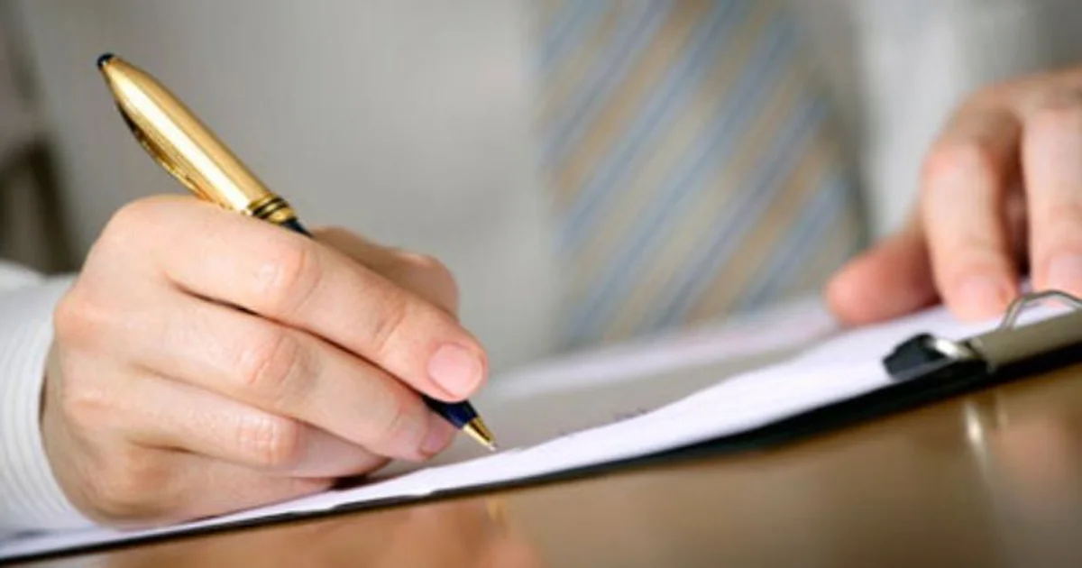 شخص يوقع على مستند رسمي بقلم ذهبي في مشهد يعبر عن توقيع العقود والإقرارات القانونية