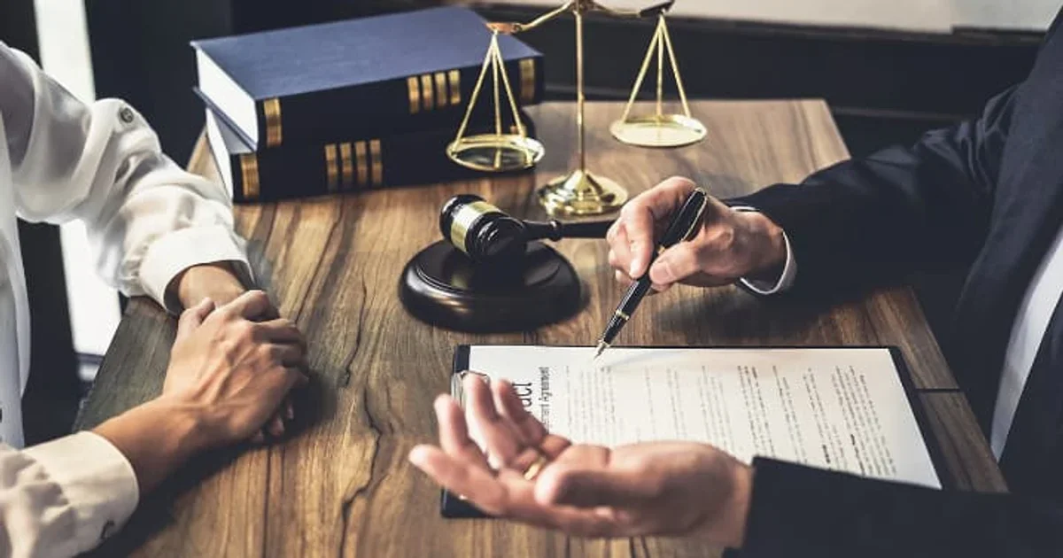 محامٍ يشرح مستندات قانونية أمام موكل داخل مكتب محاماة، مع ميزان العدالة ومطرقة المحكمة، في مشهد يعبر عن الاستشارة القانونية وتنظيم حقوق الزوج والزوجة في مسائل الميراث.